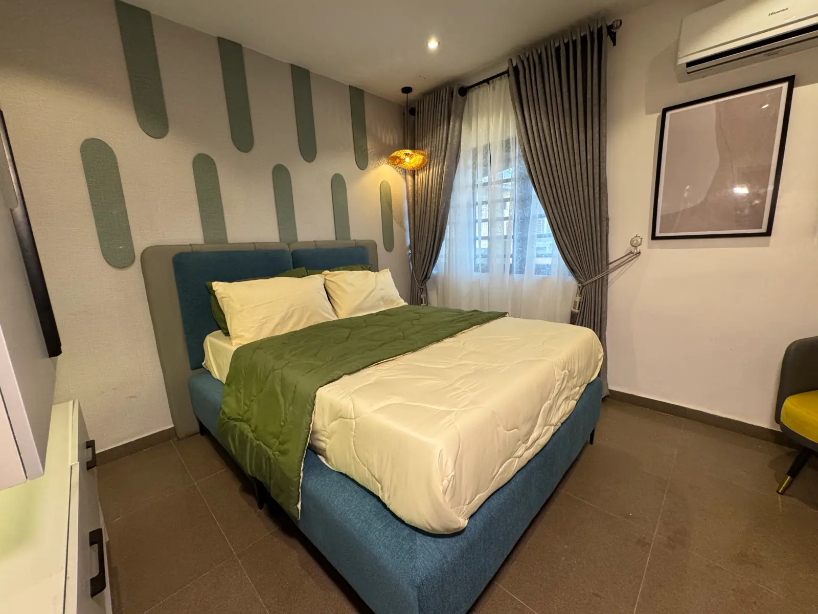 Bedroom with a dusty-blue headboard, green and cream bedding and sage capsule shapes on the wall