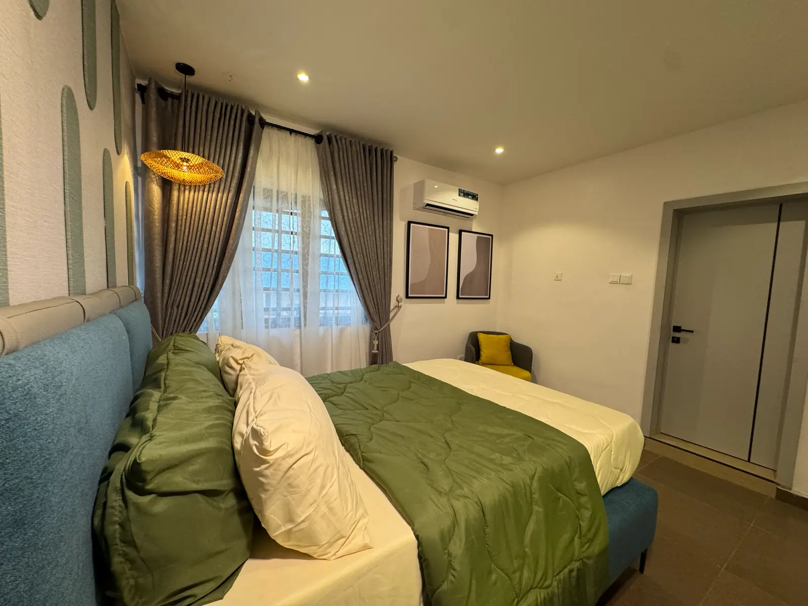 The blue bedroom from the foot of the bed, with grey curtains and a yellow chair