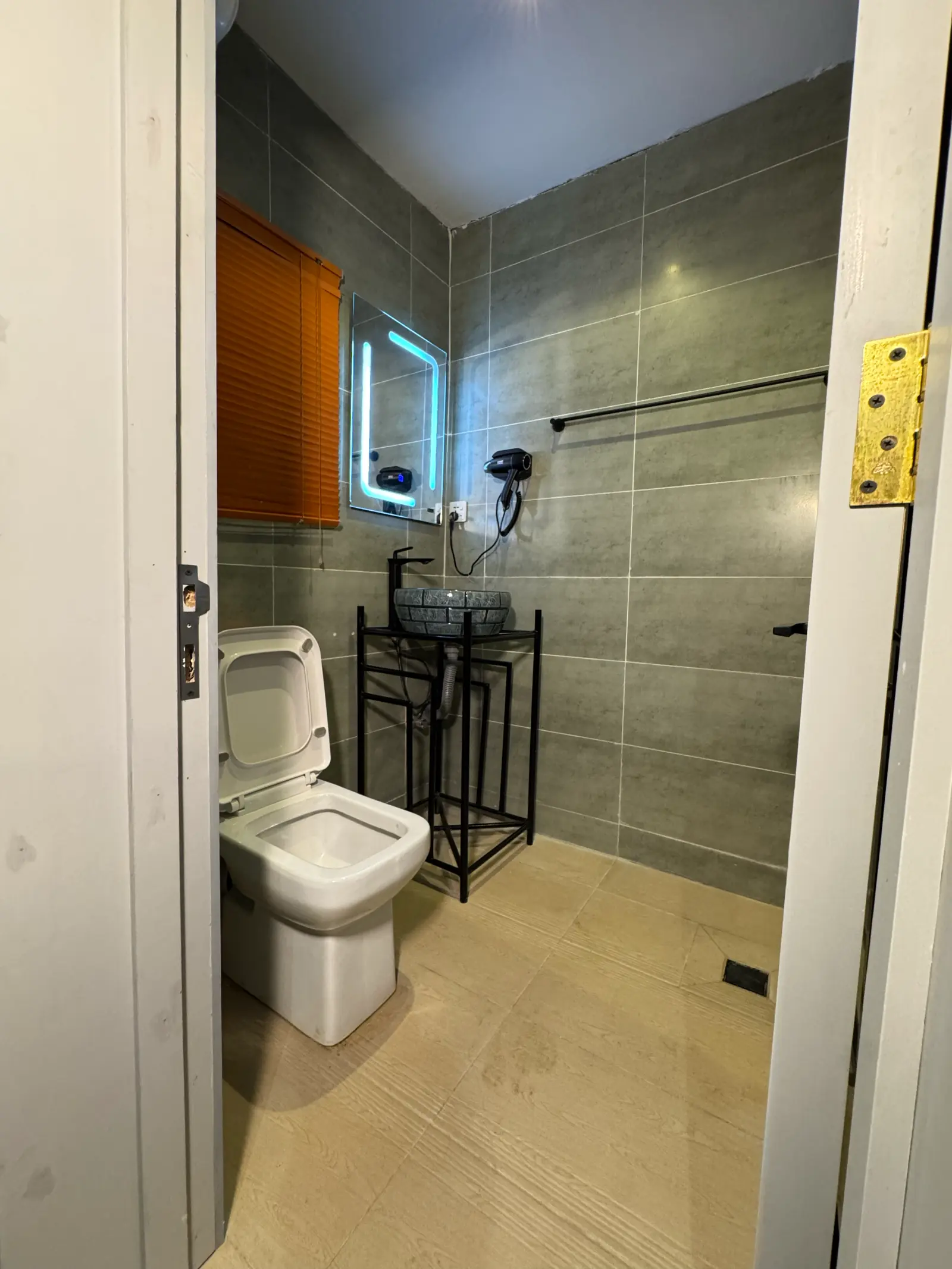 Bathroom seen from the door: a glass shower with green tiles, a basin and an orange blind
