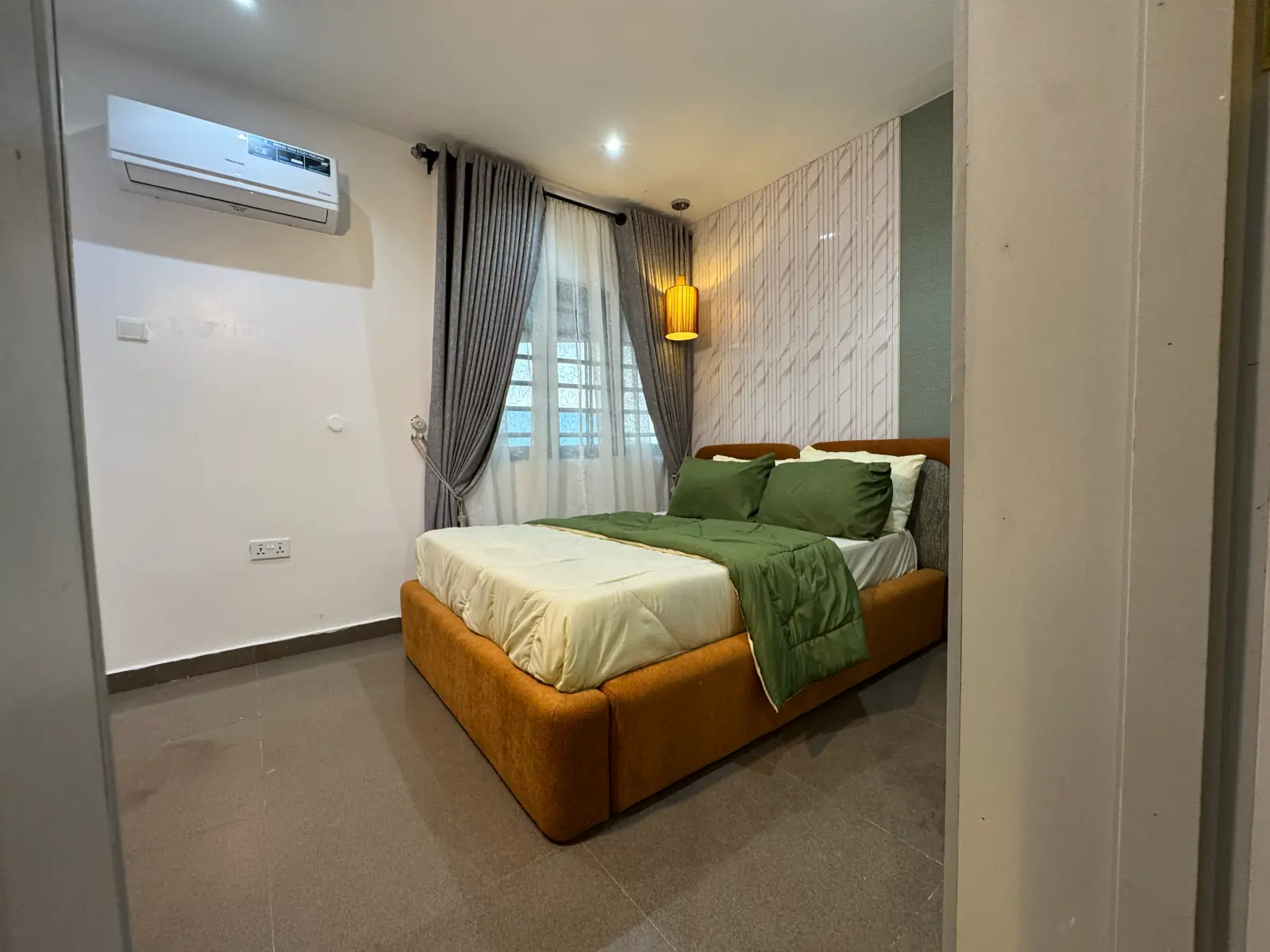 Bedroom with a tan upholstered bed, green throw and grey curtains