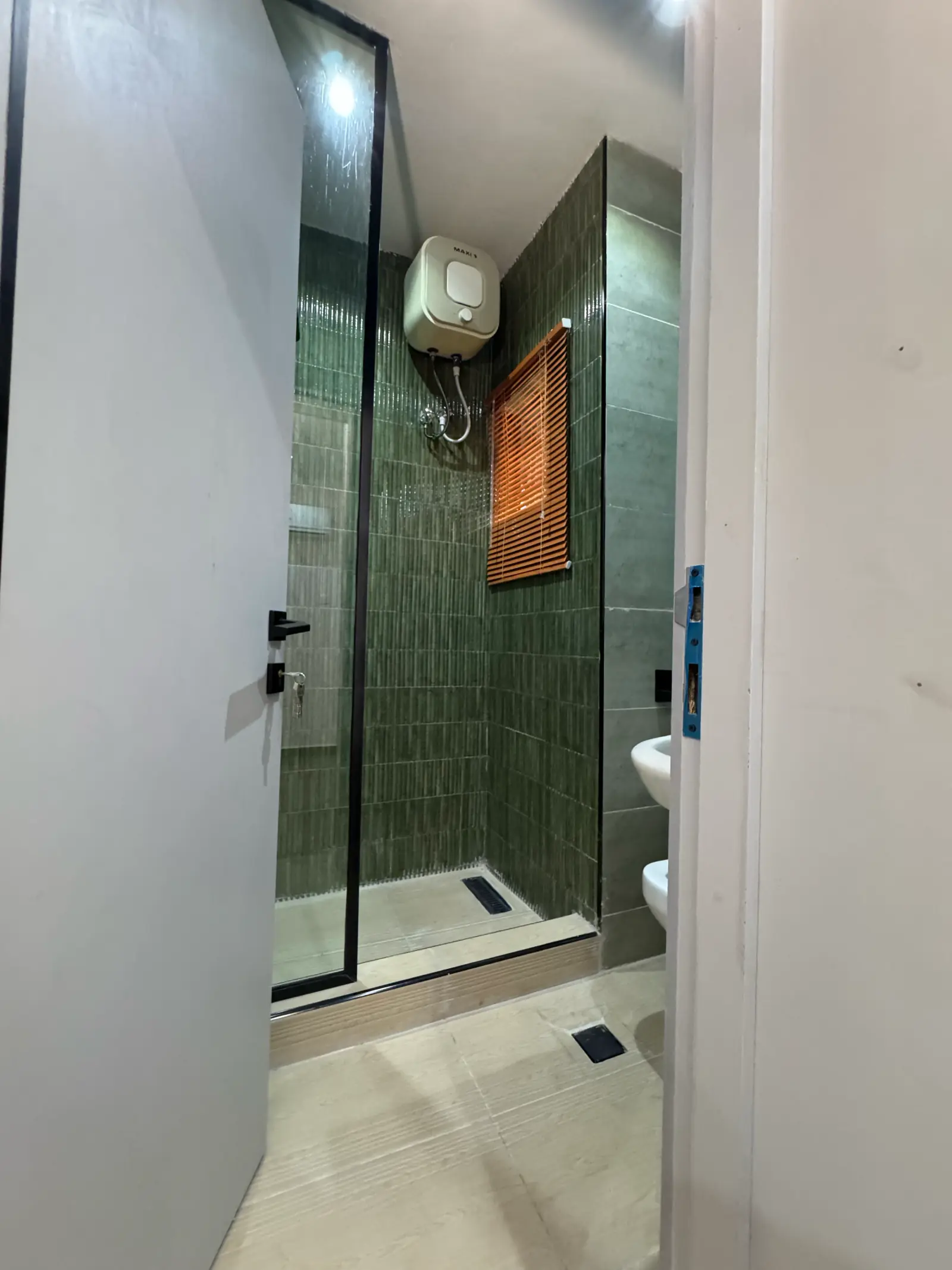 Shower with deep green vertical tiles behind a glass screen